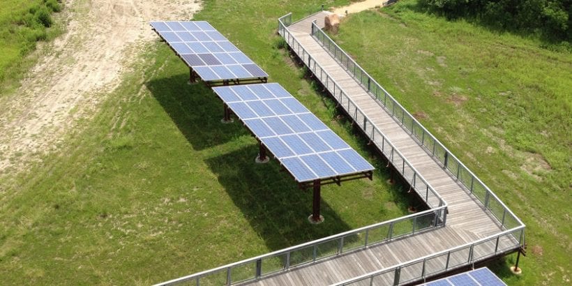 Row of solar panels sitting next to an elevated walking path.